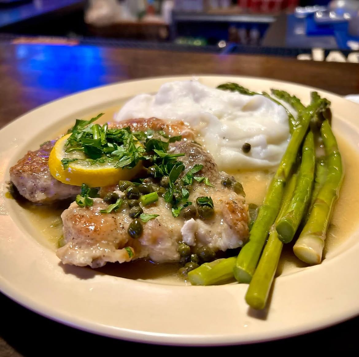 Chicken piccata in lemon caper sauce with mashed potatoes and asparagus on a white plate