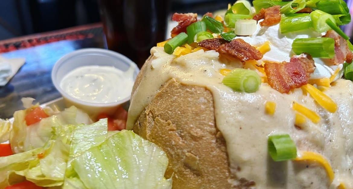 A baked potato loaded with cheese, bacon, spring onion and sour cream, served with a side salad