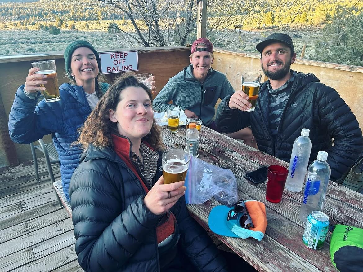 Four hikers raising glasses around a weathered picnic table on the deck
