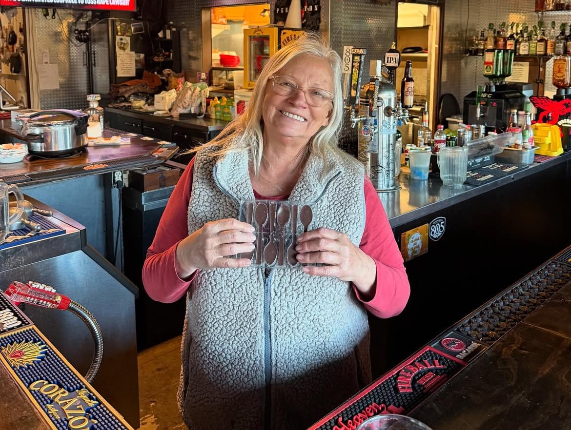 A member of staff behind the bar, shelves of bottles behind her