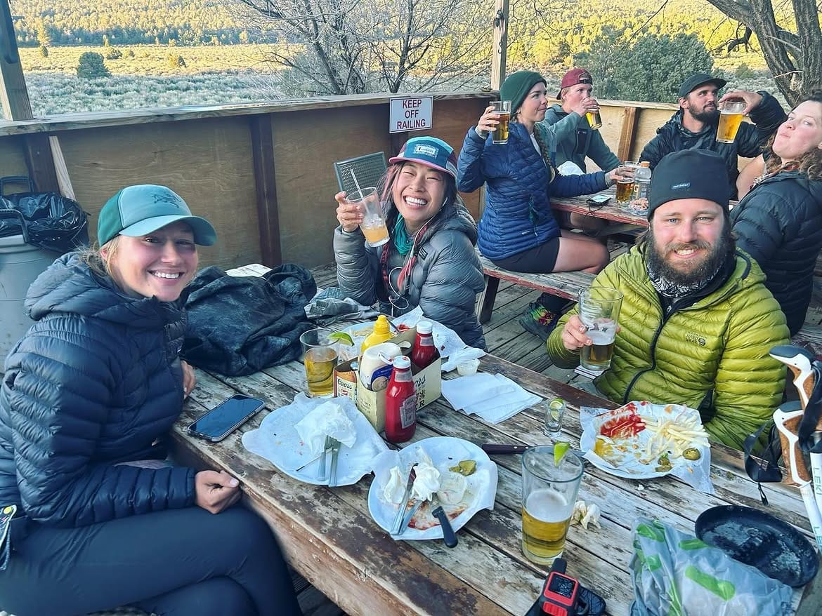 Hikers eating at the outdoor picnic tables, the meadow beyond