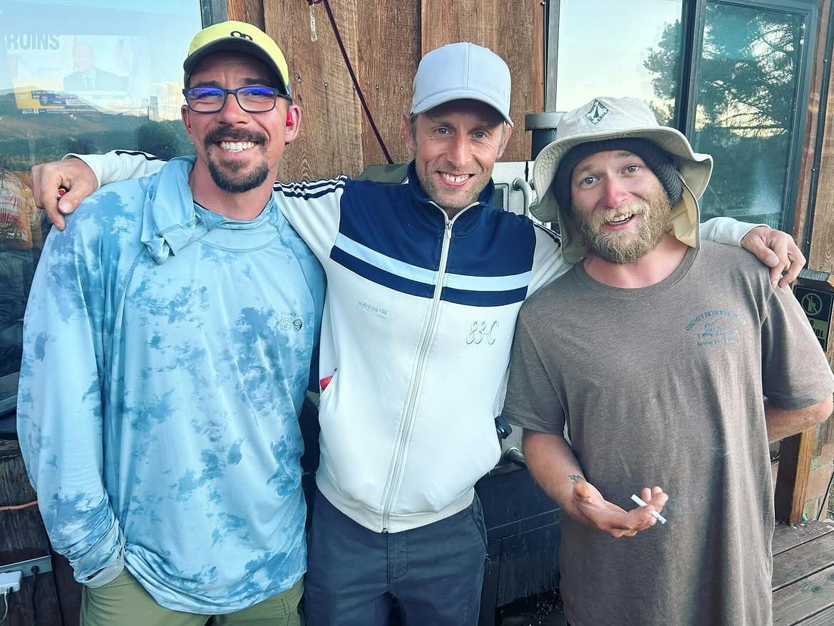 Three hikers arm in arm in front of the timber wall